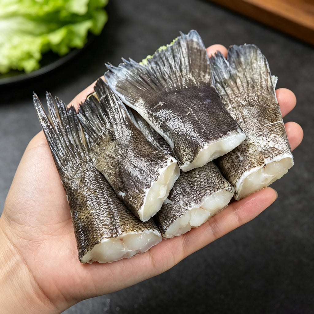Hand holding raw cod fish tails with grey skin and white flesh