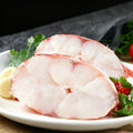 Raw red rockfish fillet on a white plate with herbs